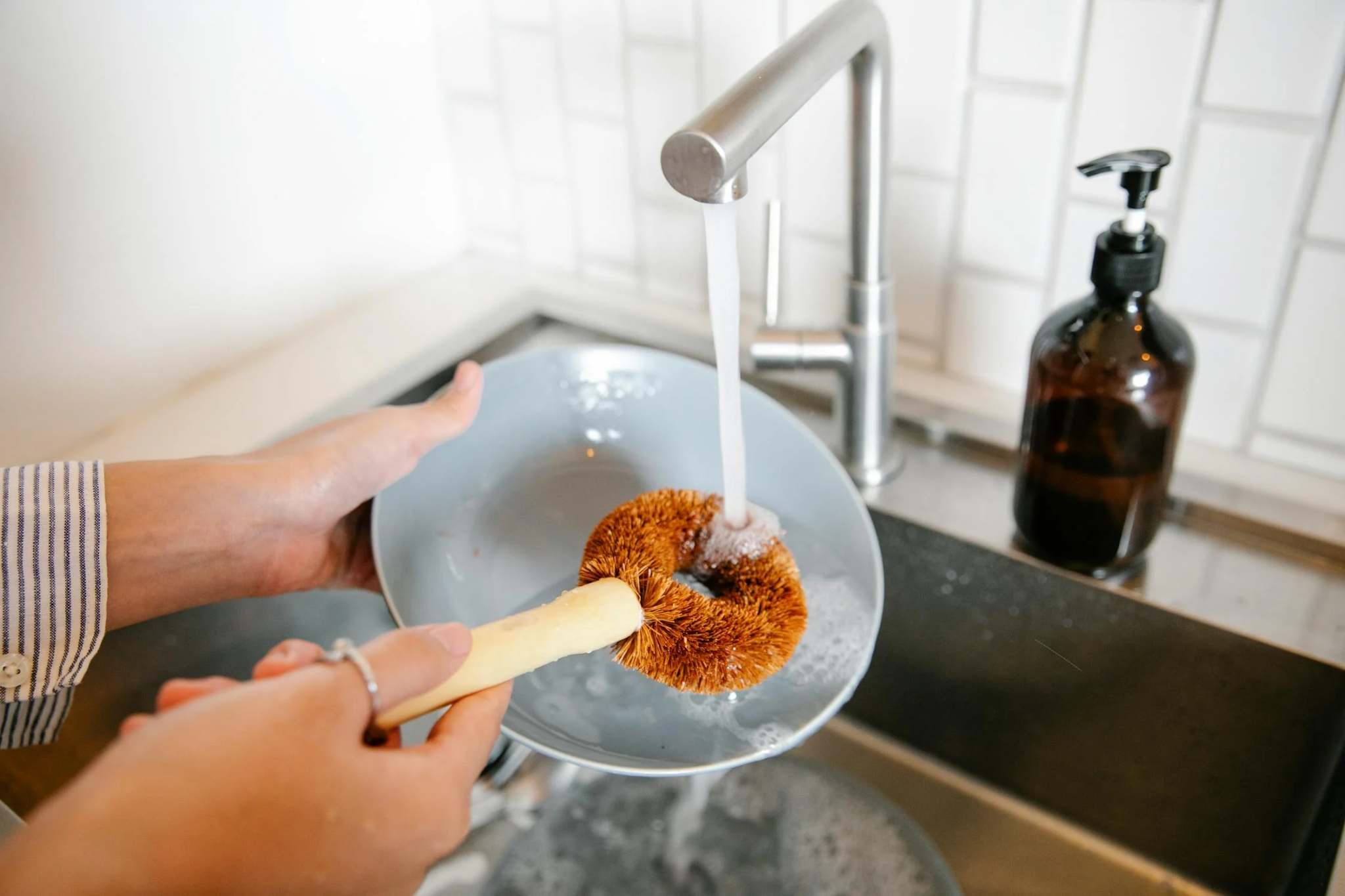 A person washes a dish in their kitchen sink.