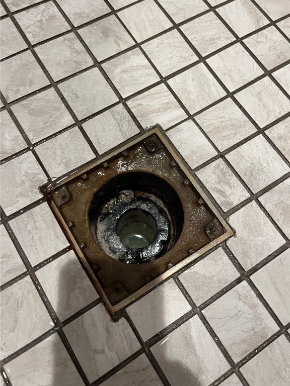 A heavily clogged shower drain showing buildup and residue, likely causing slow drainage or backups