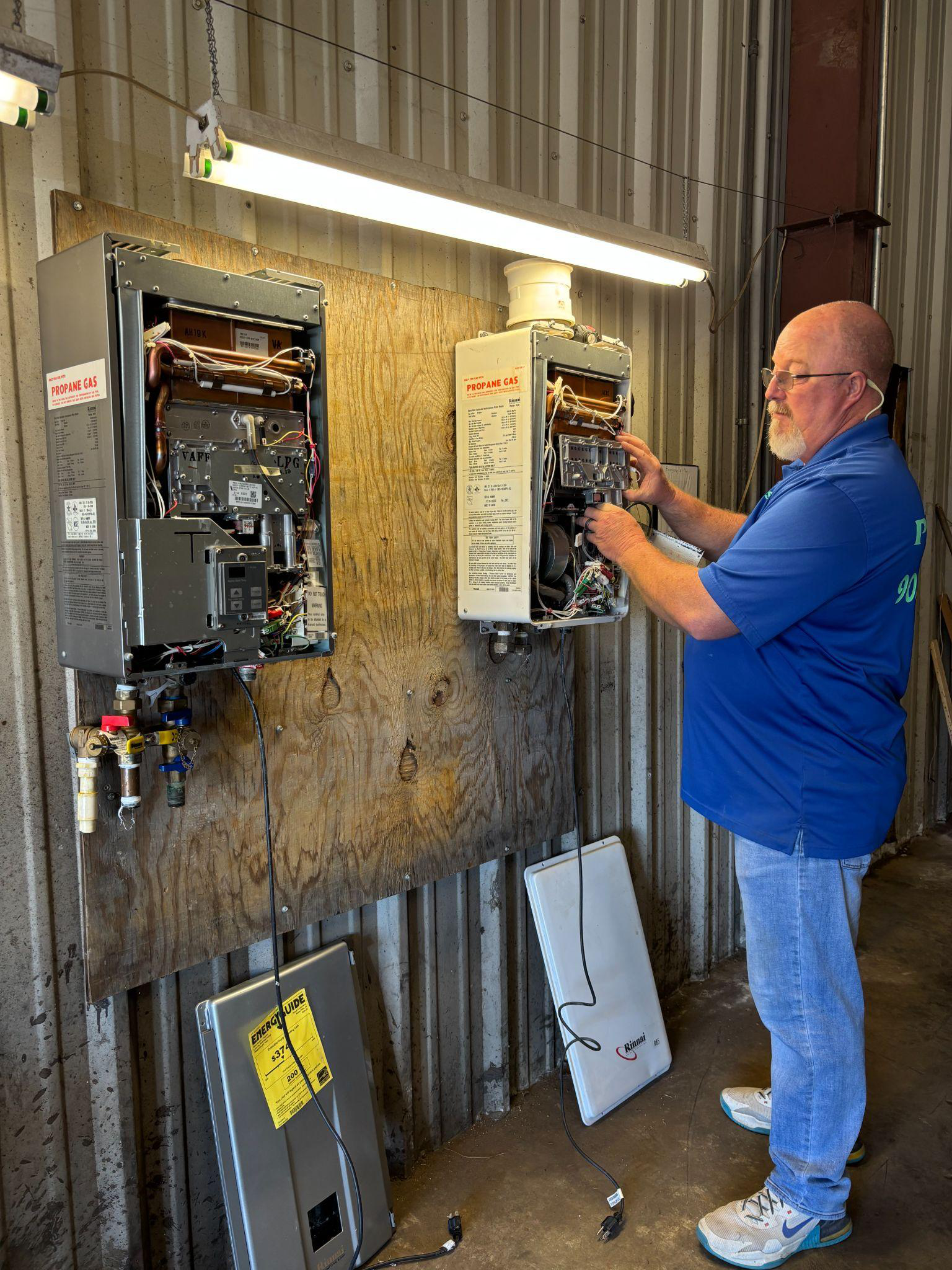 Technician from Acute Plumbing Care performing preventive maintenance on two mounted water heaters in a workshop setting.