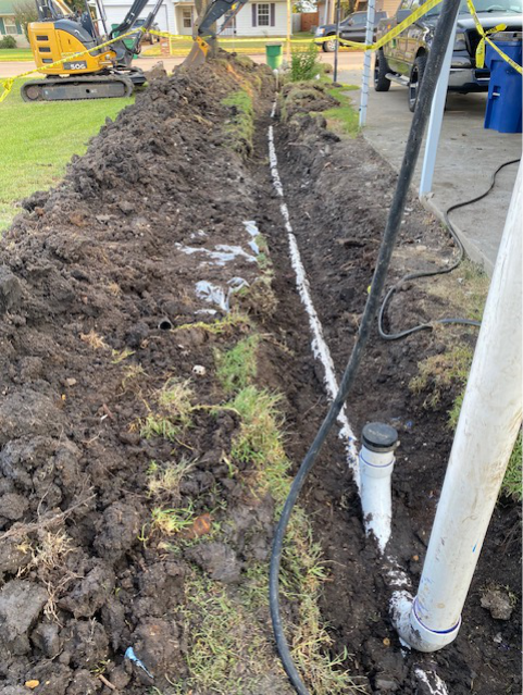 Excavated trench exposing a replaced sewer line after tree root damage.