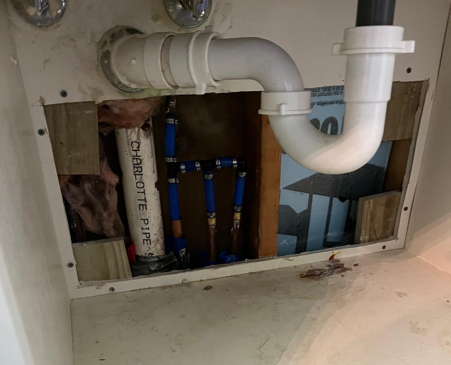 Exposed plumbing system under sink showing potential leak points