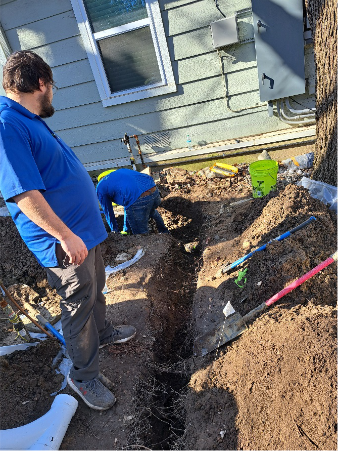 Licensed plumbers performing excavation work to repair underground plumbing near a home exterior