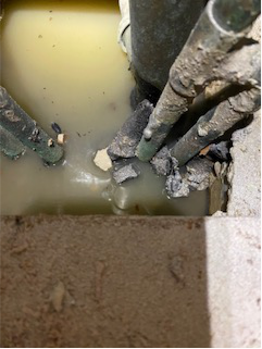Standing water pooling around corroded pipes in a hidden cavity