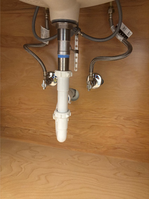 View of plumbing connections under a bathroom sink with visible P trap and supply lines